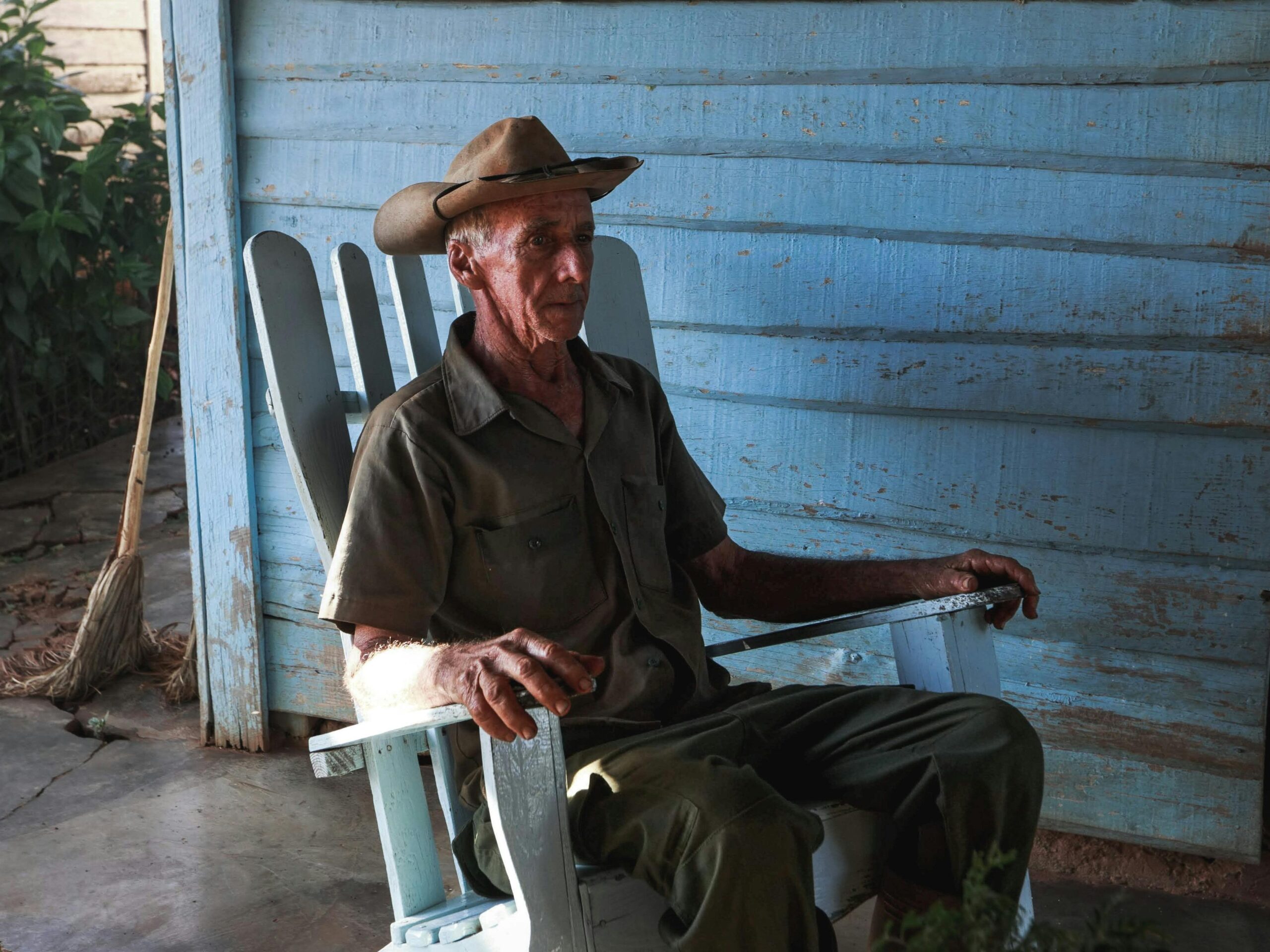 Senior man wearing cowboy hat sitting in wooden rocking chair outdoors.