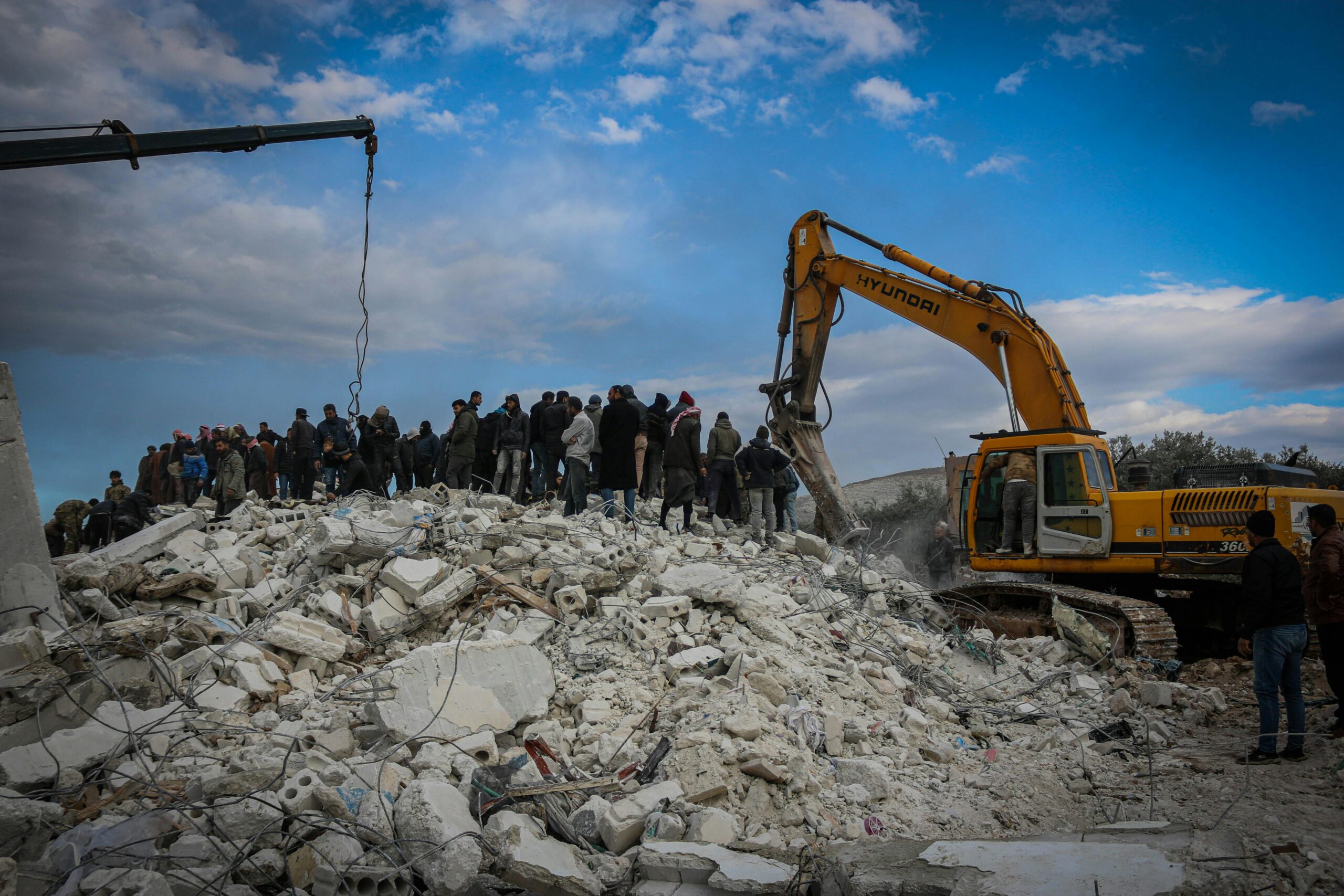 Rescue workers and excavator at disaster site in Idlib, Syria, removing debris.
